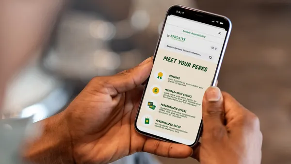 Close-up of a hand holding a phone with a grocer’s app on the screen with details on its loyalty program, such as personalized offers and member-only events.