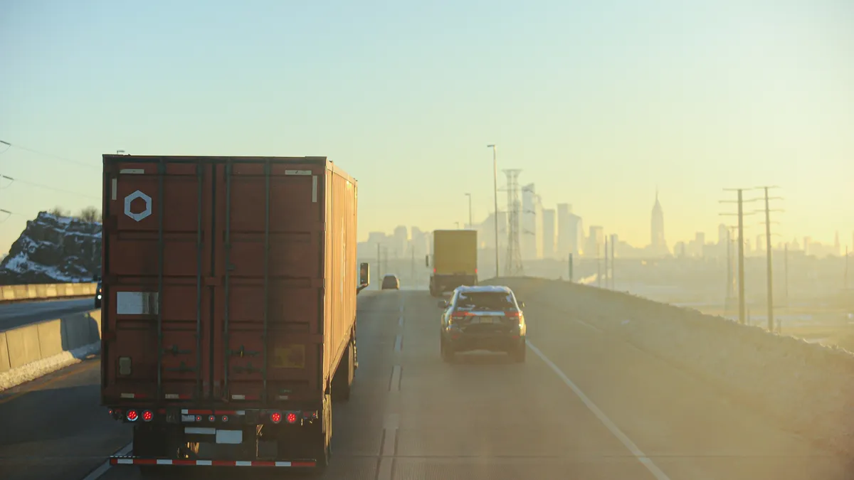 Trucks and passenger vehicles on a bridge with the Empire State Building in the background.