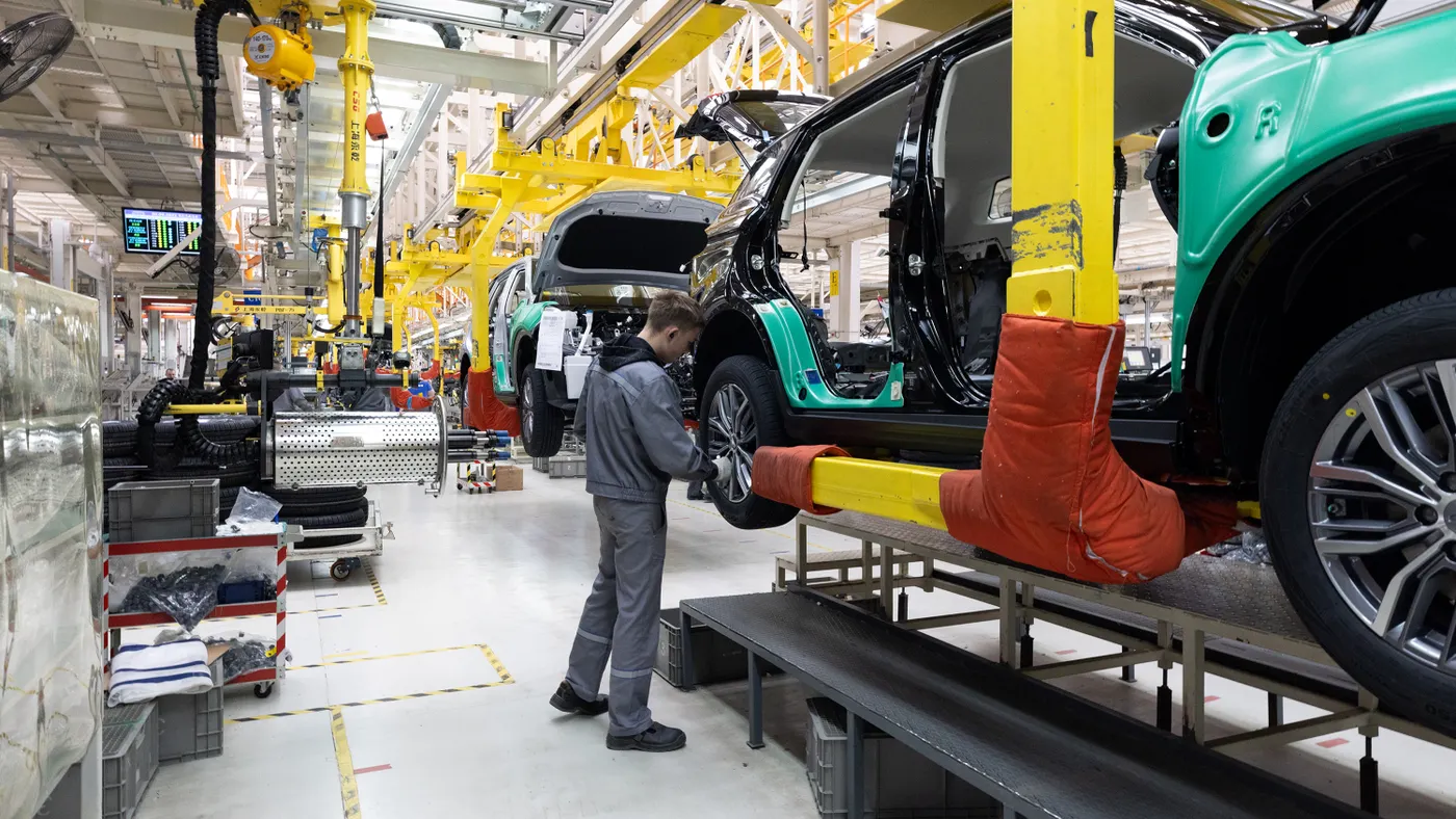 Worker inspecting car on assembly line in automotive factory.