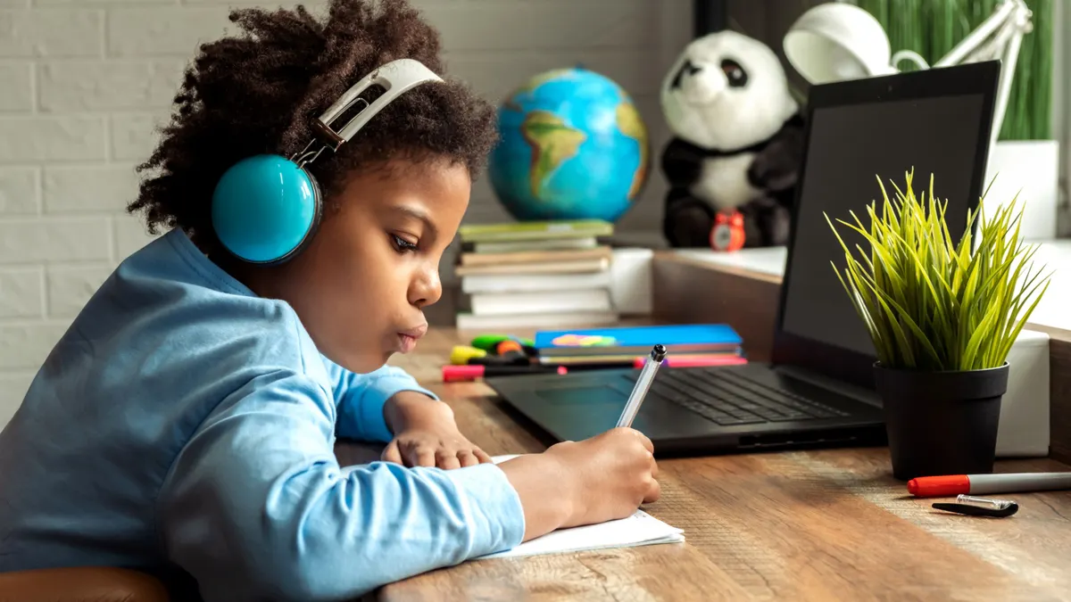 A young student completes their homework in front of their computer while sitting at a desk at home.