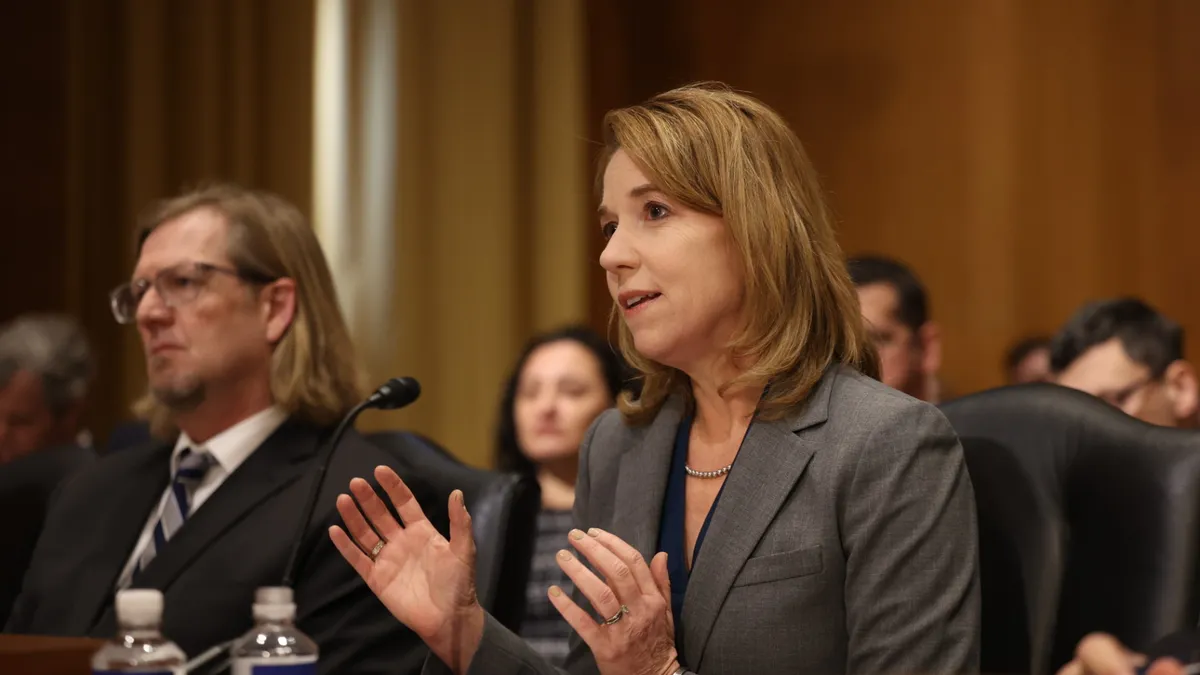 National Multifamily Housing Council president Sharon Wilson Géno sits in a chair among many other people and speaks into a microphone.