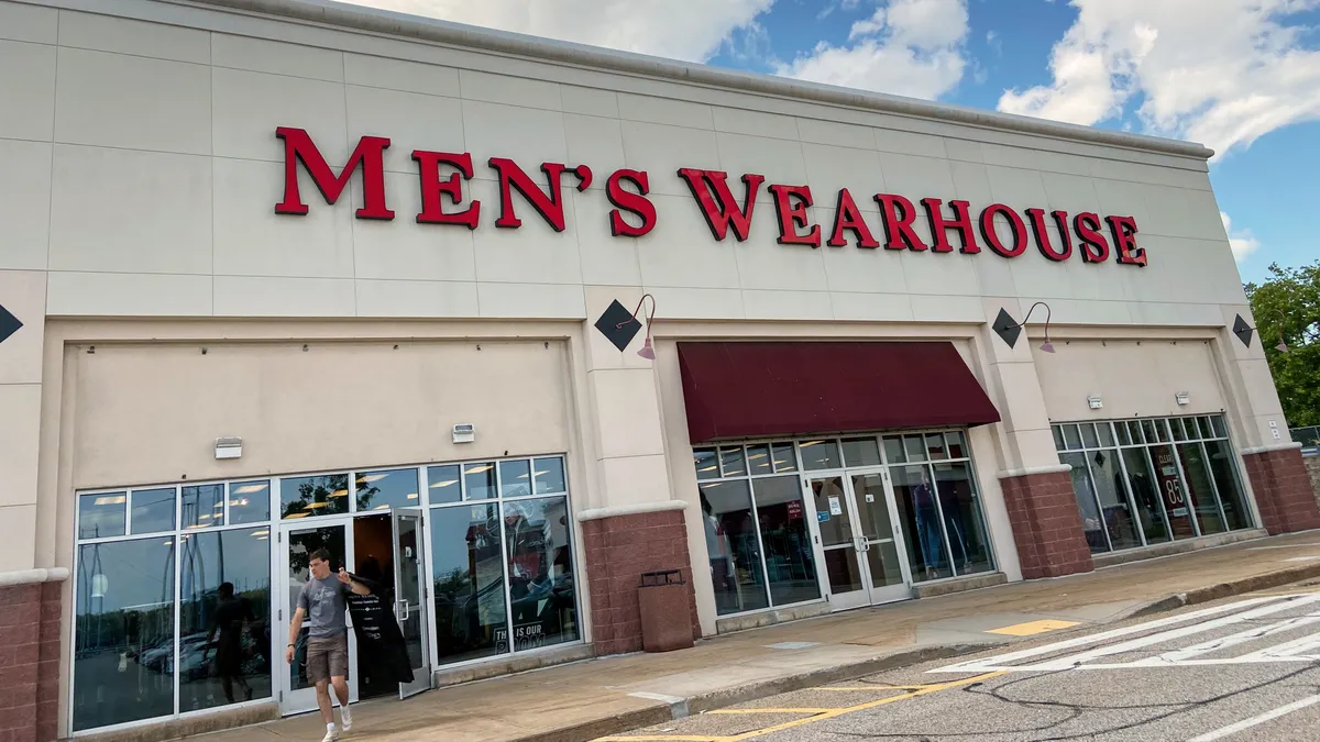 A customer walks out of a store carrying a suit slung over the shoulder.