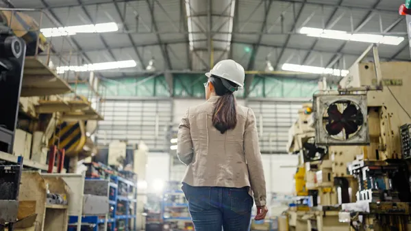 A factory worker stands with their back to the camera in a factory setting.