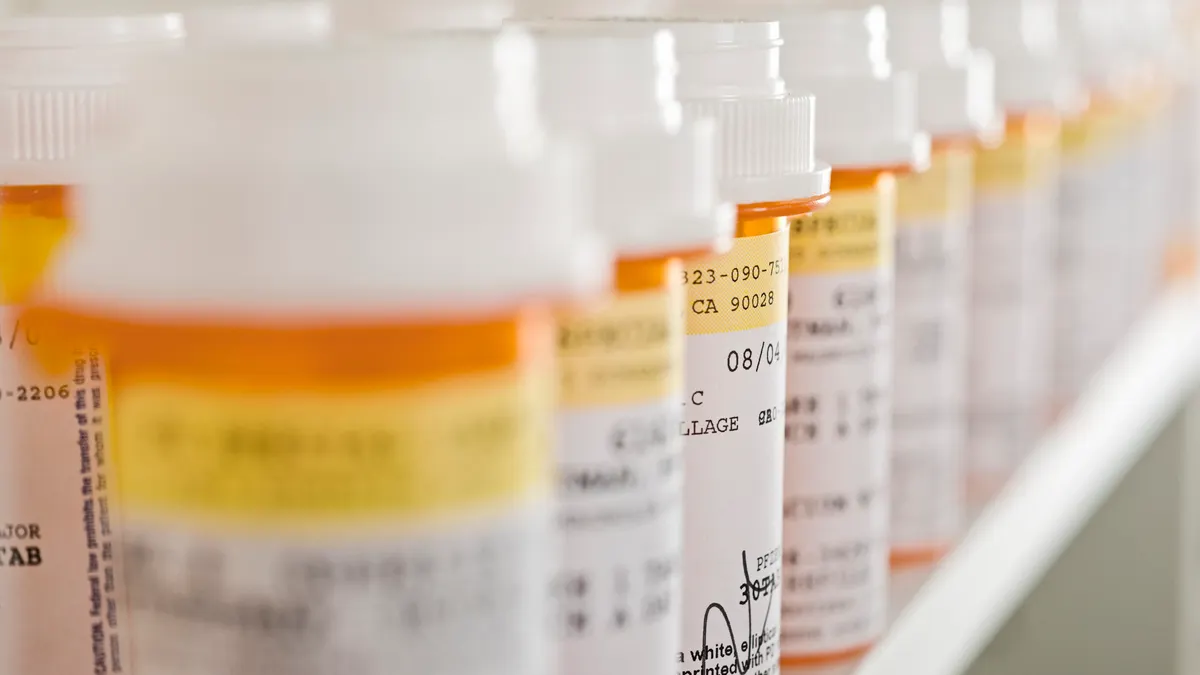 Various pill bottles stand arranged on a pharmacy shelf.