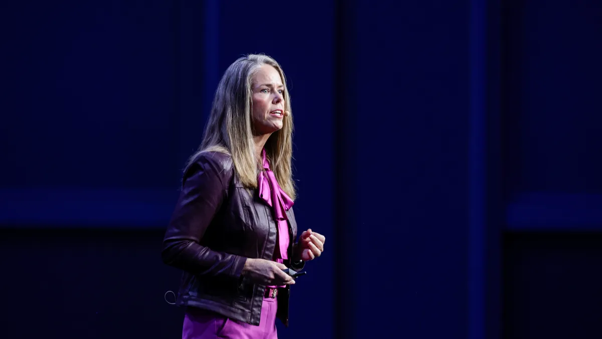 Mandi Bishop speaks during a conference in front of a blue screen