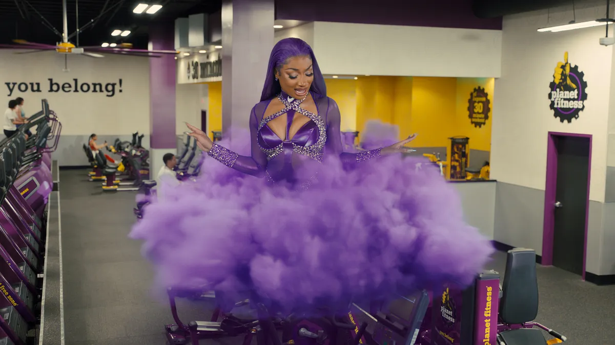 Megan Thee Stallion floats in a cloud of purple above gym equipment in a Planet Fitness.