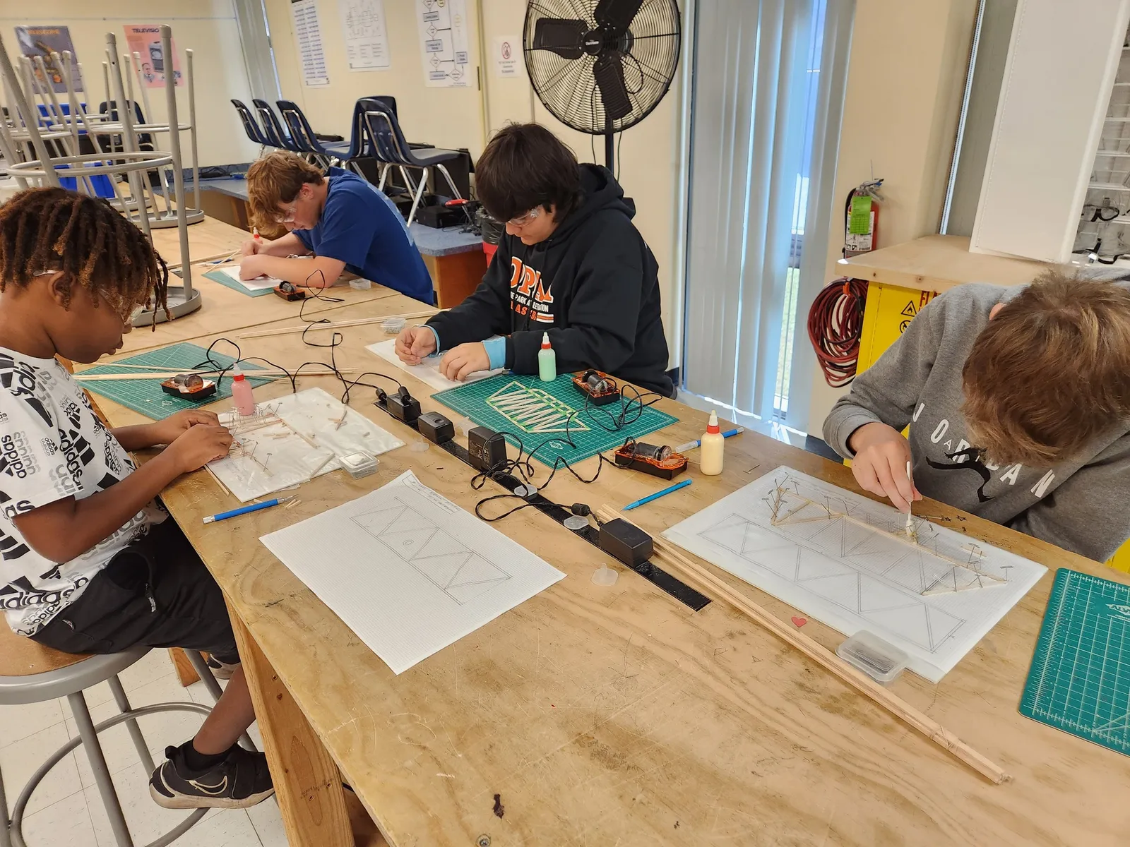 Students sit at a large table and work on engineering projects.