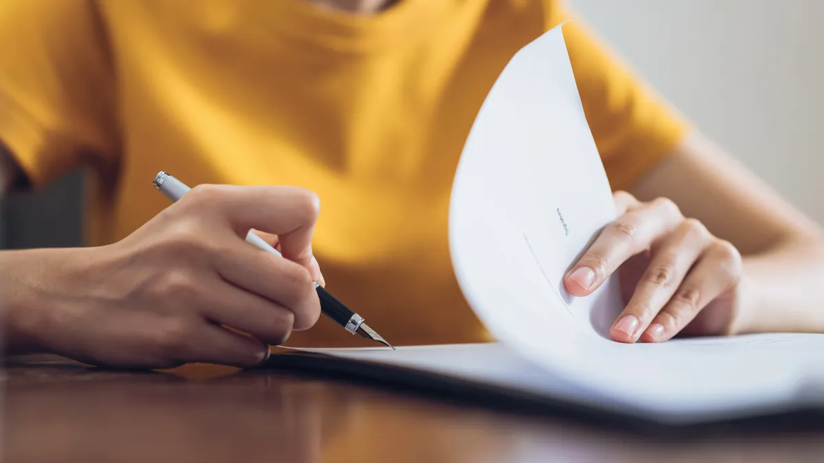 A person writes with a pen on a stack of papers.