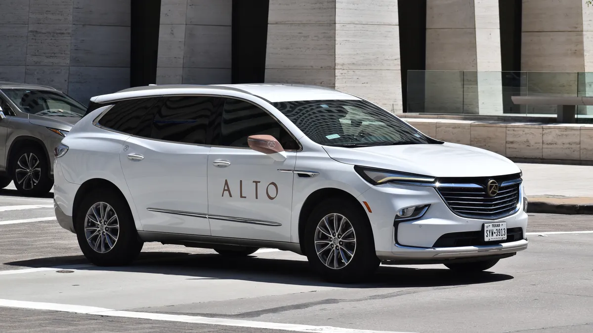 A white Buick Enclave luxury SUV used as an official Alto company car, cruising in a downtown district.