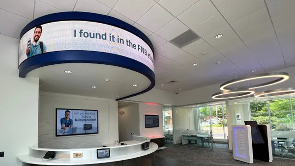 The interior of a new First National Bank branch is shown, with screens reading "I found it in the FNB eStore" and "Are you working hard to build your credit?"