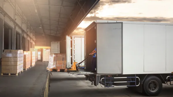Worker loading package boxes on pallets into cargo container at dock warehouse