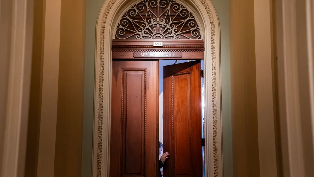 Two large wooden doors slightly opened. Within the opening is pictured a person looking into the room.