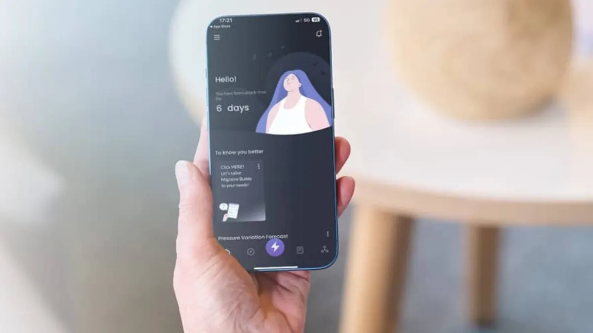 A hand holds a smartphone displaying an app with a calming design, featuring an illustration of a relaxed person and weather forecasts. Background is softly blurred.