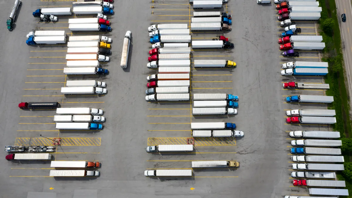 Dozens of white trailers connected to different tractors, shown in red, blue, yellow and other colors, are shown in a parking lot at a truck stop.