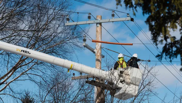 Two electric utility workers in a cherry picker prepare to work on the wires of a power pole.