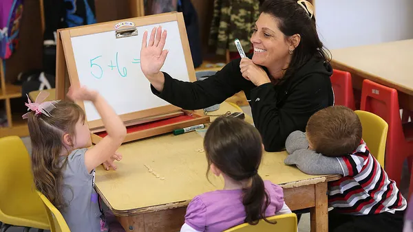 An adult sits at a table with young children. The adult high 5s one child