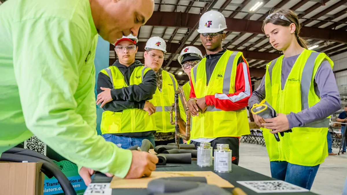 Several young people in high-vis construction safety gear gather around a table.