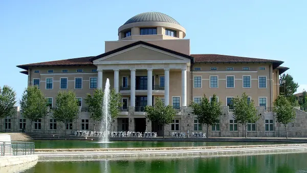Administration building with columns and a modern dome in front of a large decorative pond.