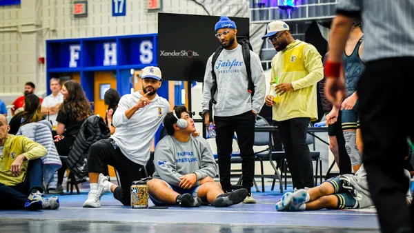 Coaches talk with a wrestler during a tournament in a school gym