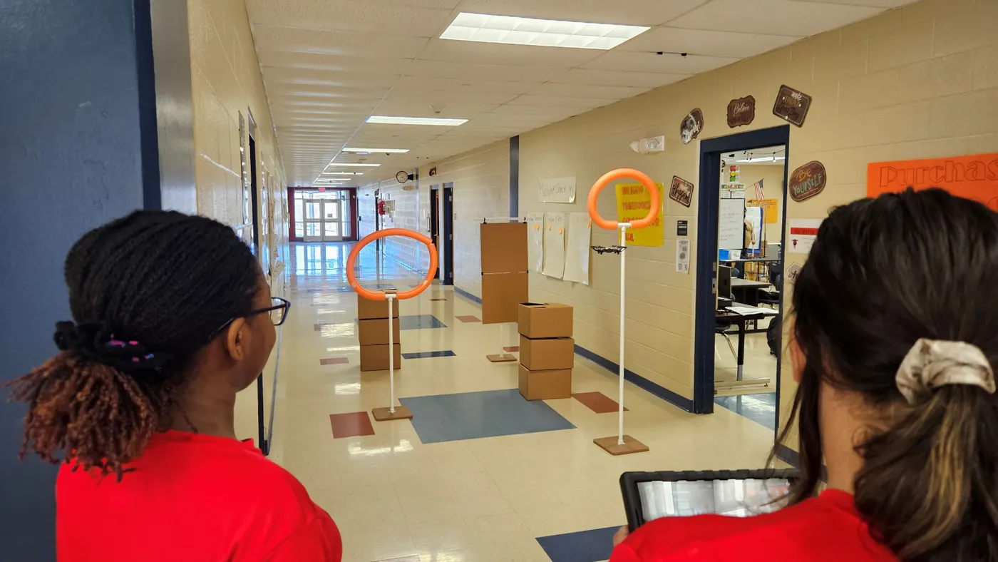 Two students in a school hallway looking at tall white metal poles with orange circles standing at the top of poles.