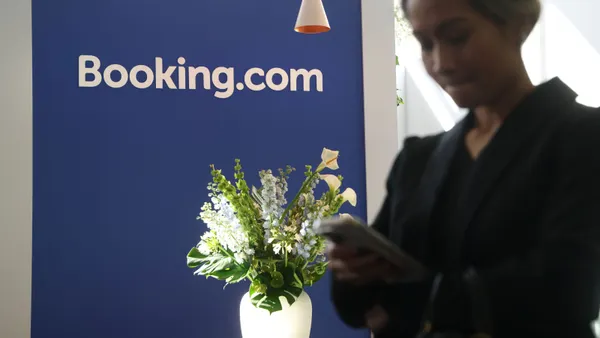 A person uses their phone in front of a Booking.com sign.