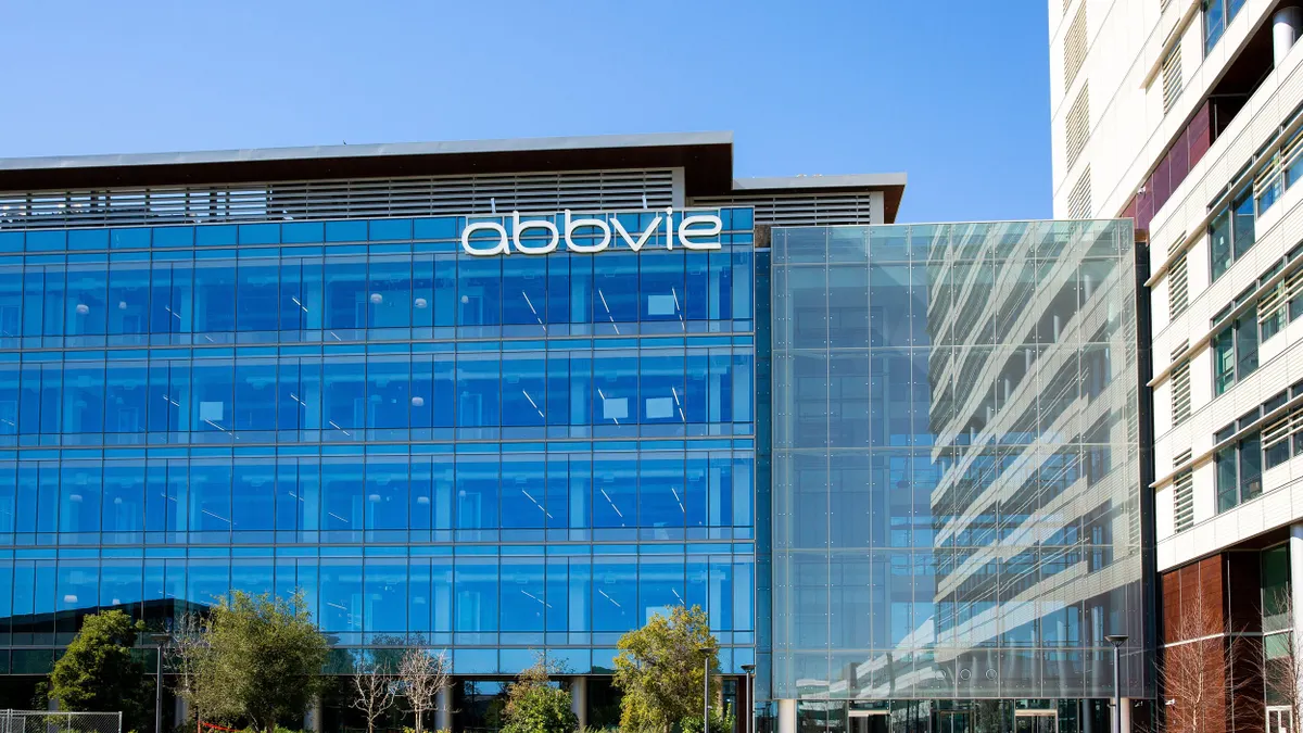 An all-blue glass facade with the "AbbVie" logo is mounted to the top of the building, and another commercial building surrounds the building. 