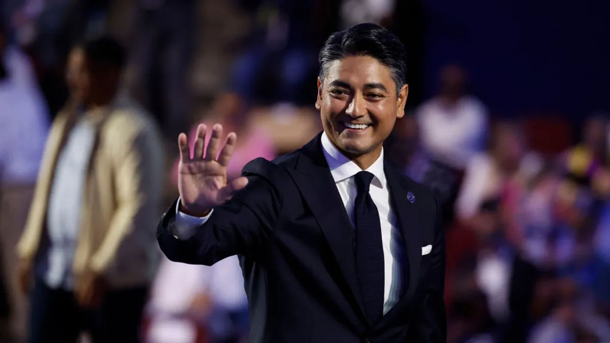 A person in a suit and tie waves in front of a crowd.