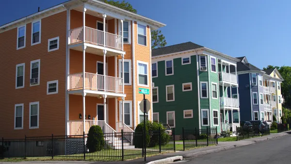 Three three-story homes with three balconies each line a city street.