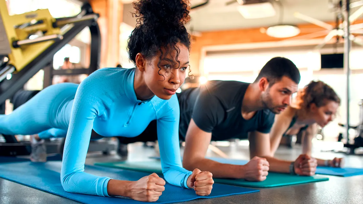 A line of three people do planks on gym mats at a gym.