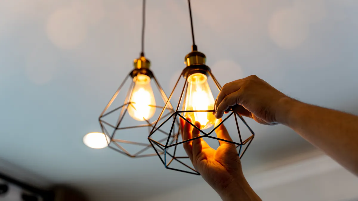 A closeup of a hand belonging to an electrician installing electric LED lightbulbs on a ceiling.