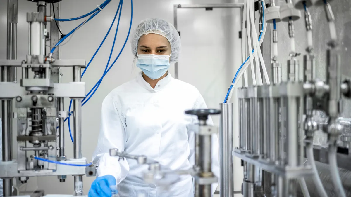 A worker in protective gear operates a high-tech machine which streamlines pharmaceutical production.