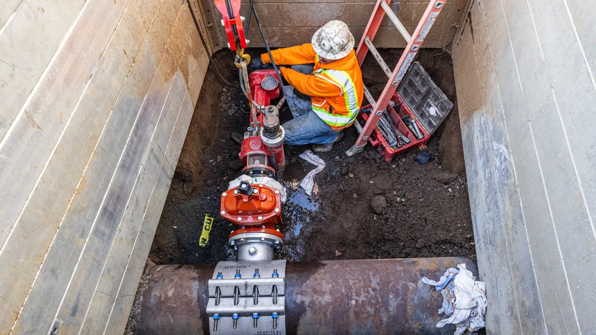 Person wearing a yellow uniform working underground on pipes.