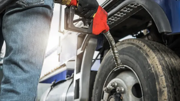 A truck driver prepares to refuel a truck while holding a diesel pump nozzle.