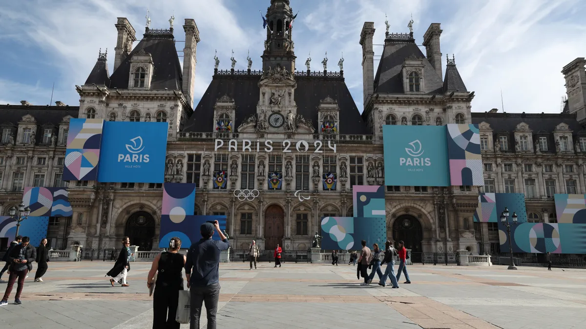 Paris town hall draped with the city's 2024 Olympic logo and a plaza with people.