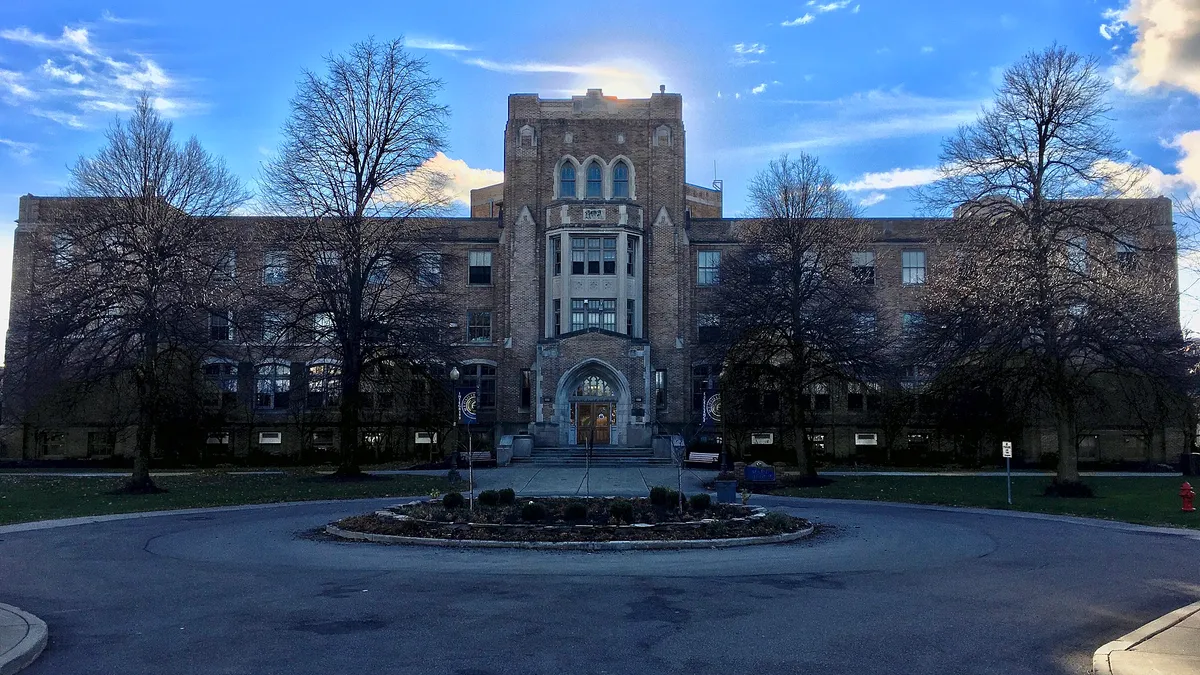 A large brick academic building partially silhouettes the sun.