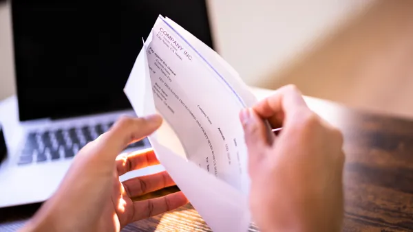 Hands holding a paycheck with a laptop in the background.