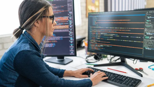 Developer coding and programming on two with screens.