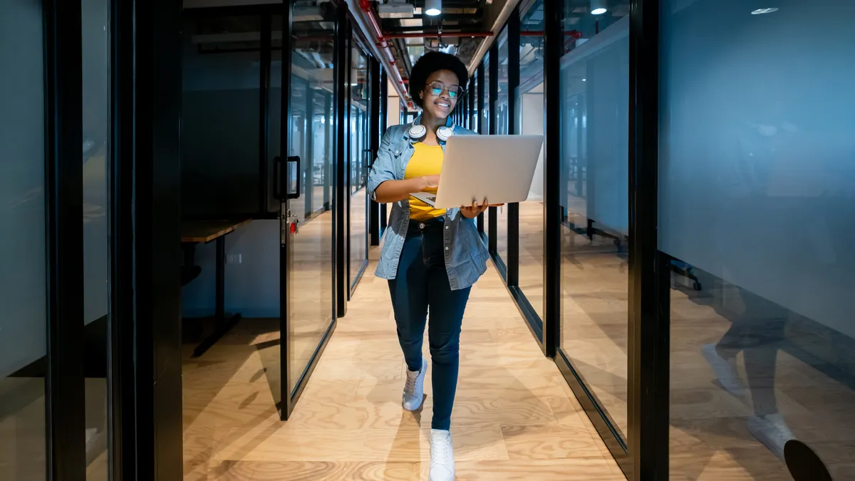 A worker walks in a tech firm office with a laptop.