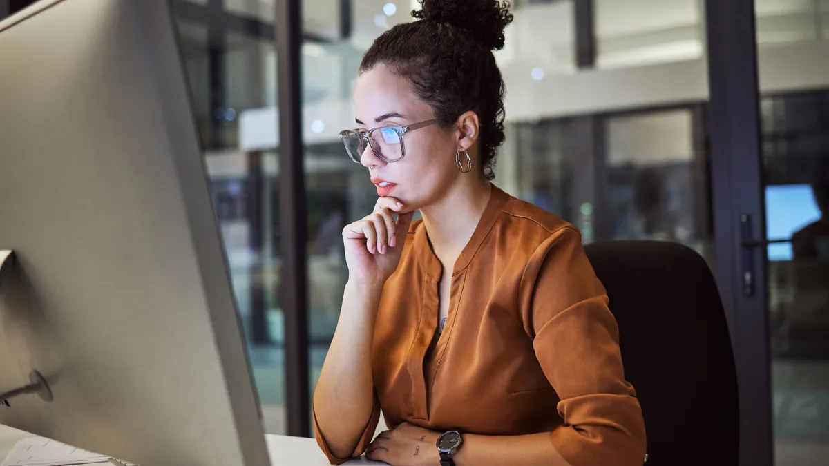 Person at desk looking confused while staring at a laptop.