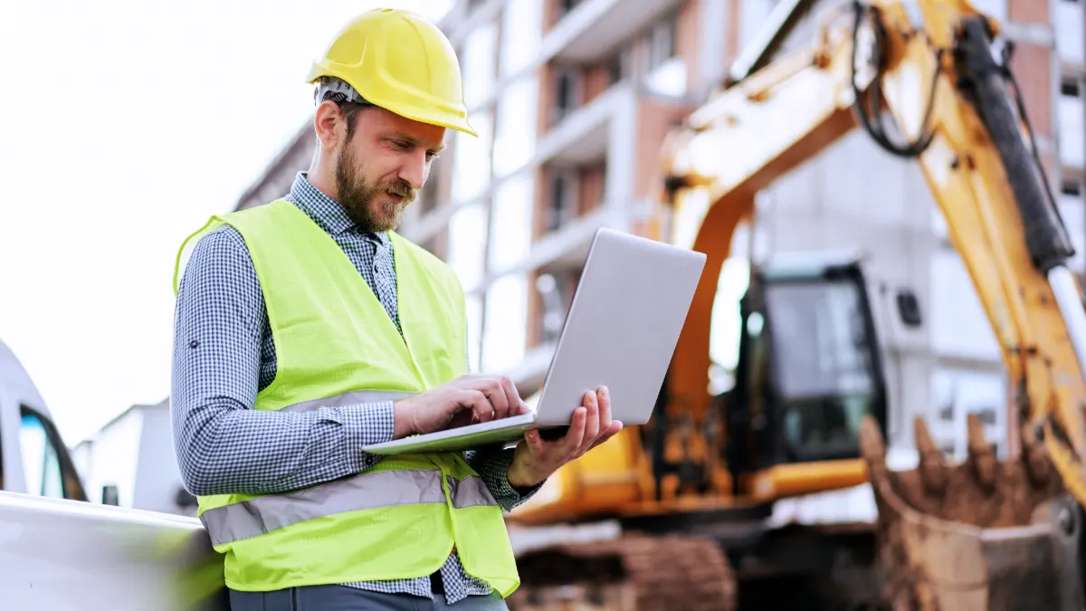 Architect standing in building in construction process and using laptop for improving blueprints