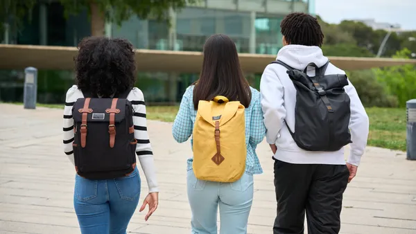 Three students with their backs turned toward the camera walk along a college campus.