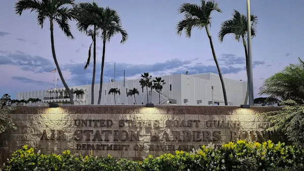 A shot of a tall building with a stone marker on the front that reads "United States Coast Guard Air Station Barbers Point Department of Homeland Security."