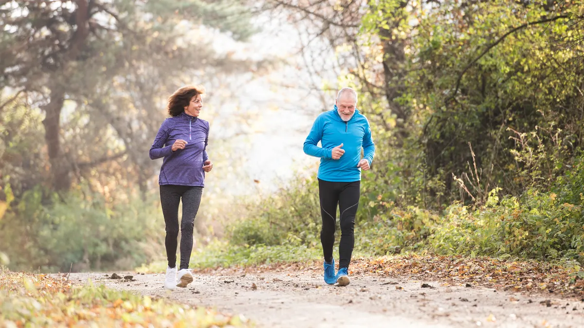 Active senior couple running together outside on a forest trail