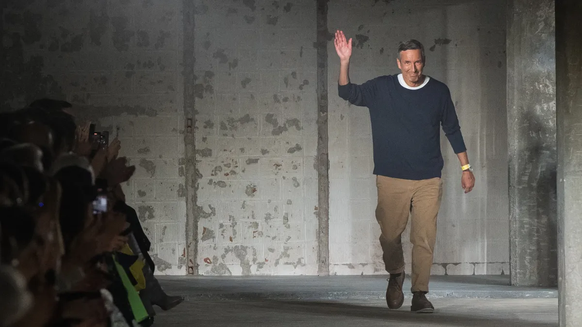 Designer Dries Van Noten waves while walking on the runway.