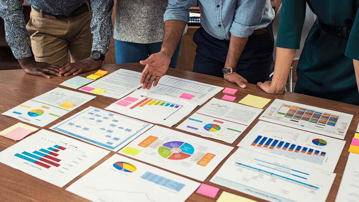 People stand around a table that holds papers showing charts and graphs.