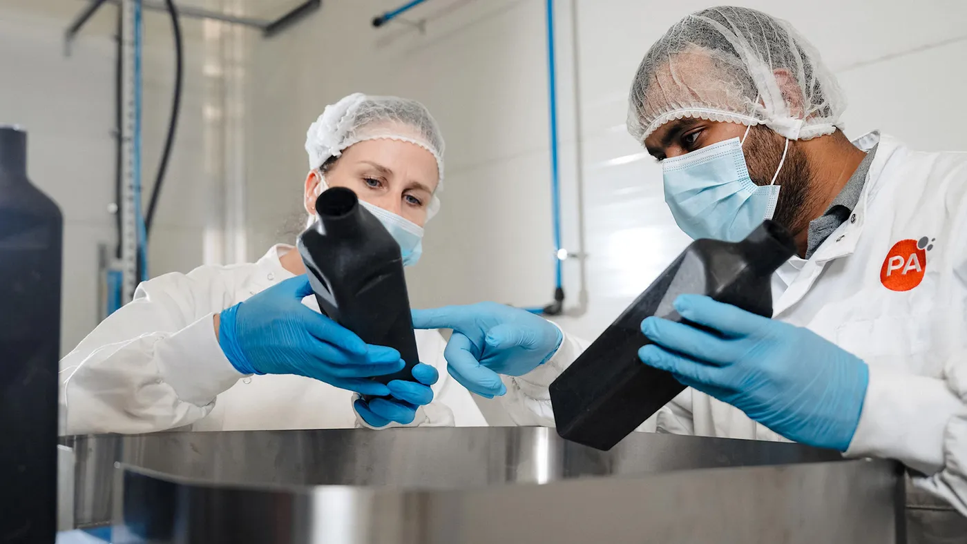 Two people wearing protective garments handle bottles of Johnnie Walker Black Label in a lab.