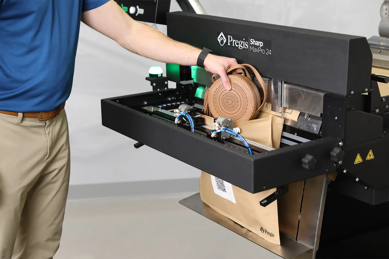 A person puts an item into a fiber mailer that is being made on a piece of industrial equipment.