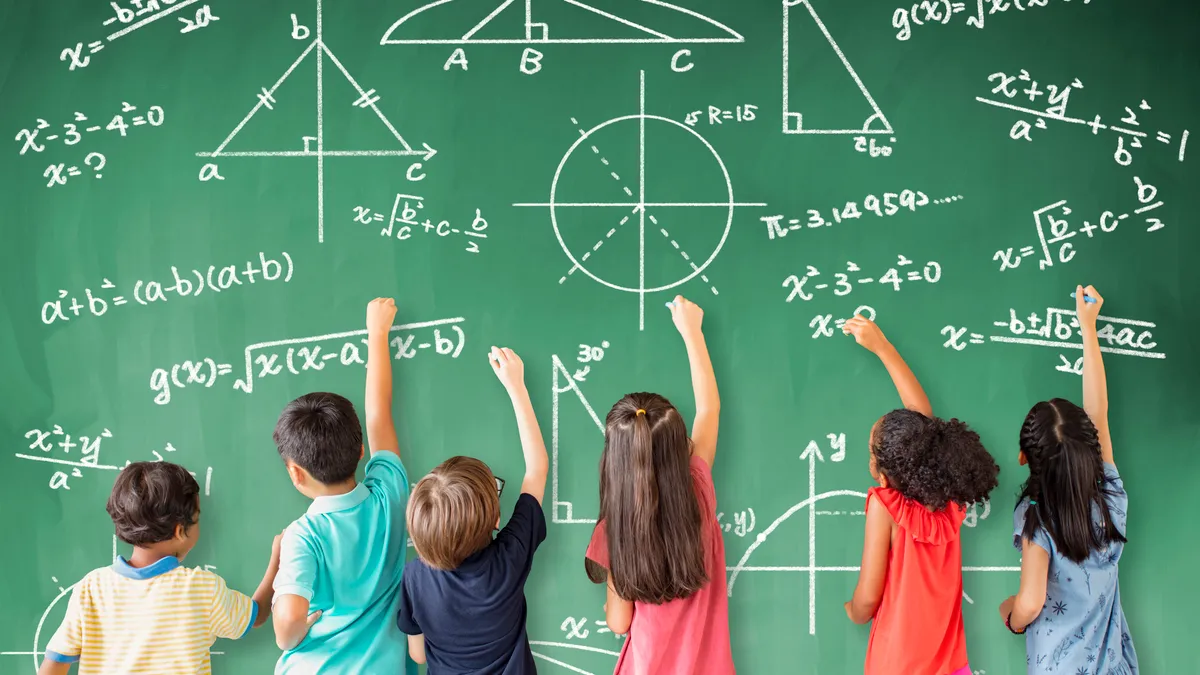 Six students face a classroom chalkboard and, with their right hands, use chalk to work on math equations.