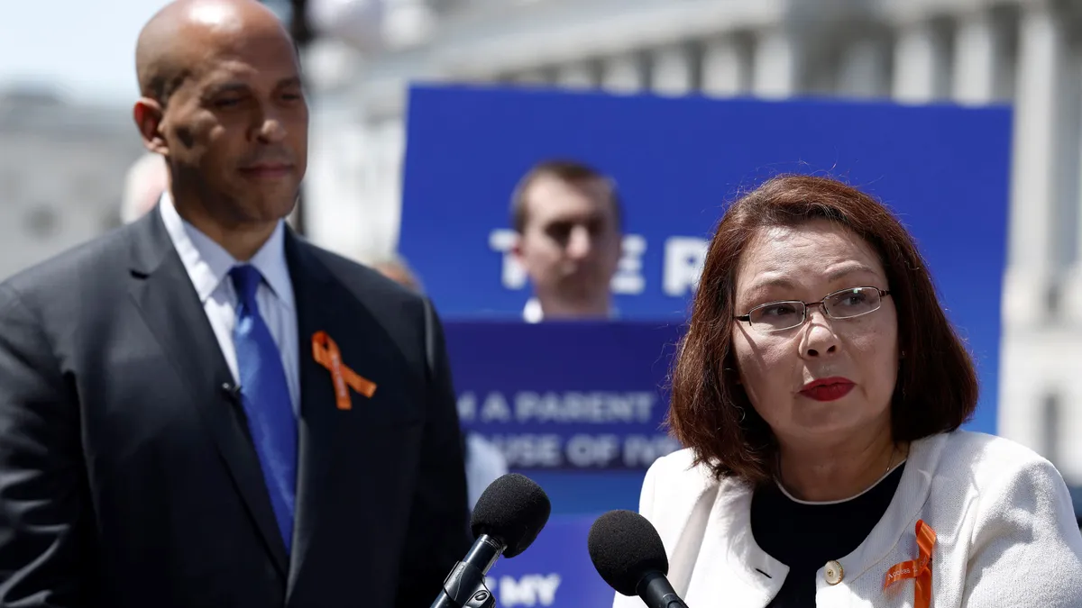 Two people stand at a podium in front of the U.S. Capitol Building.