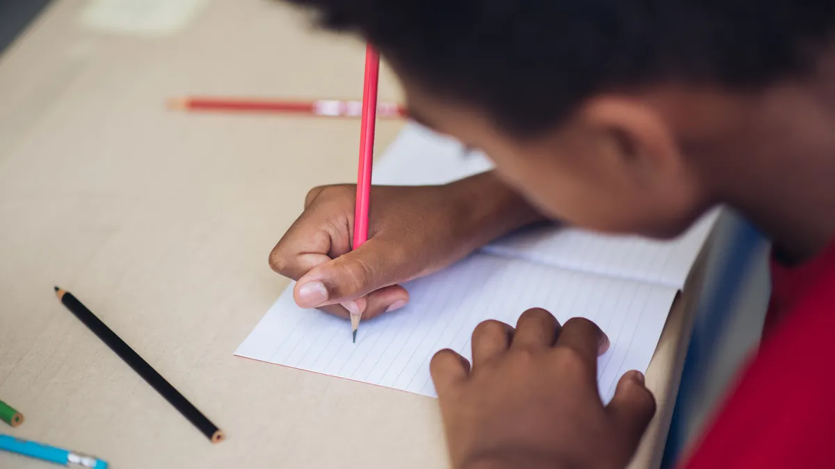 A closeup of a student's hand writing in a notebook on a desk.